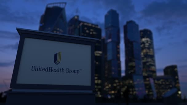 Panneau de signalisation avec logo UnitedHealth Group dans la soirée. Fond flou de gratte-ciel de quartier d'affaires. Clip éditorial 4K — Video