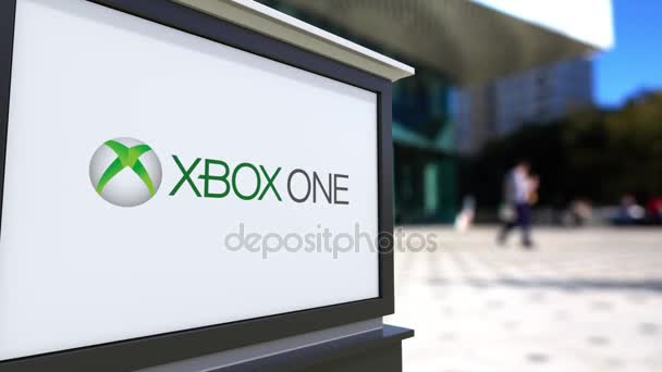 Tablero de señalización con el logotipo de Xbox One. Centro de oficina borrosa y gente caminando fondo. Representación editorial 4K 3D — Vídeo de stock