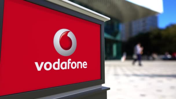 Oznakowanie ulicy deska z Vodafone logo. Centrum biurowe niewyraźne i chodzenia osób tła. Redakcji 4k renderowania 3d — Wideo stockowe