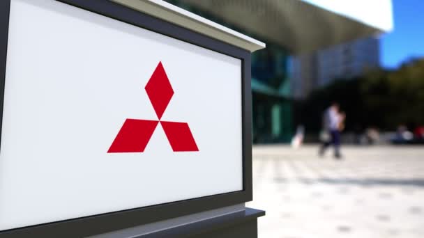Tablero de señalización con el logotipo de Mitsubishi. Centro de oficina borrosa y gente caminando fondo. Representación editorial 4K 3D — Vídeos de Stock
