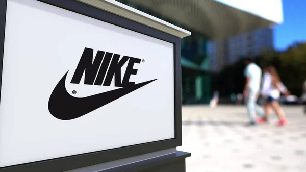 Papan nama jalan dengan tulisan Nike dan logo. Kantor pusat yang kabur, latar belakang orang berjalan. Perenderan 3D Editorial — Stok Foto