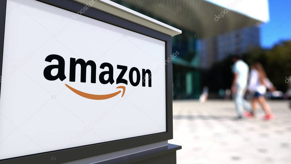 Street signage board with Amazon.com logo. Blurred office center and walking people background. Editorial 3D rendering United States