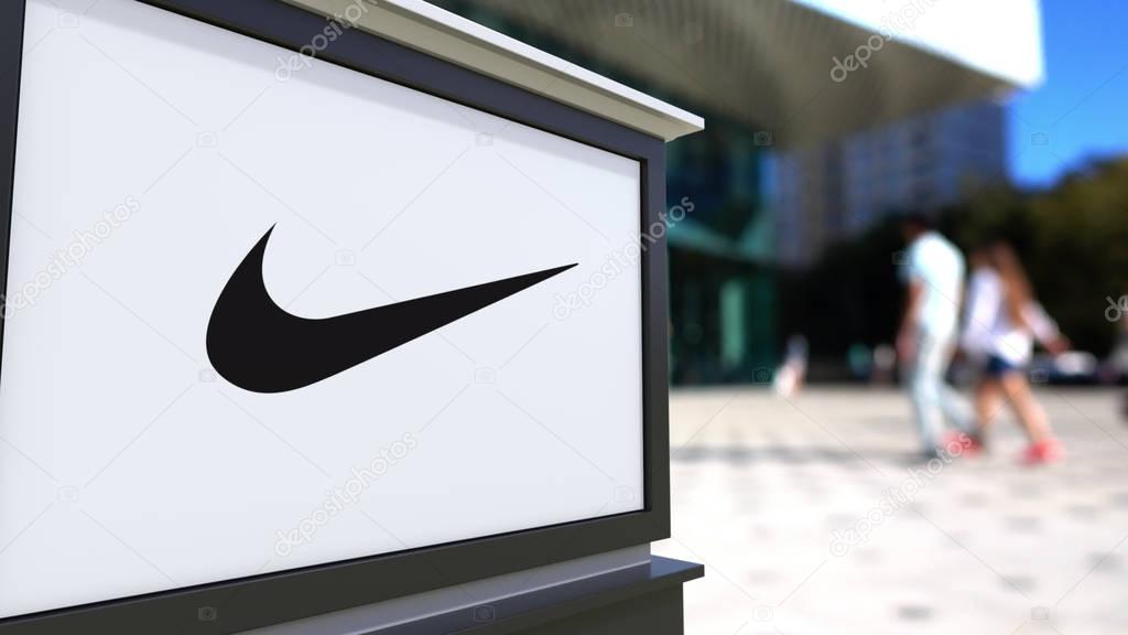 Street signage board with Nike logo. Blurred office center and walking people background. Editorial 3D rendering United States