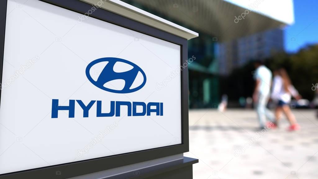 Street signage board with Hyundai Motor Company logo. Blurred office center and walking people background. Editorial 3D rendering United States