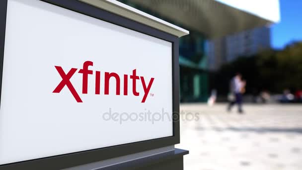 Tablero de señalización de calle con logotipo de Xfinity. Centro de oficina borrosa y gente caminando fondo. Representación editorial 4K 3D — Vídeo de stock