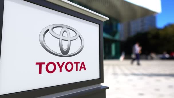 Placa de sinalização de rua com logotipo Toyota. Centro de escritórios desfocado e pessoas ambulantes fundo. Editorial 4K 3D renderização — Vídeo de Stock