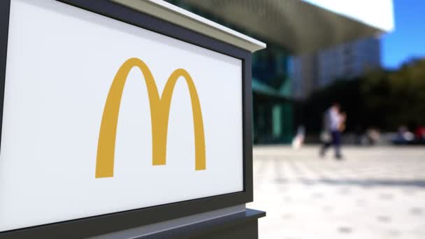 Tablero de señalización con el logotipo de McDonalds. Centro de oficina borrosa y gente caminando fondo. Representación editorial 4K 3D — Vídeo de stock