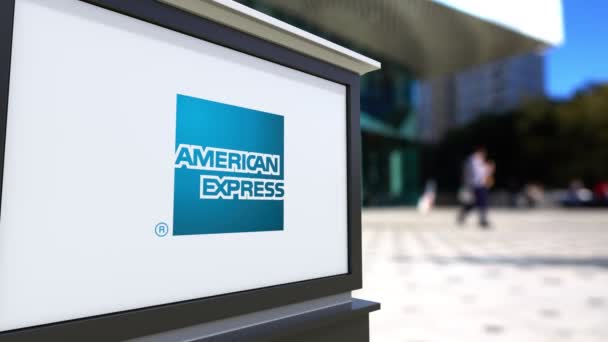 Cartelera con el logotipo de American Express. Centro de oficina borrosa y gente caminando fondo. Representación editorial 4K 3D — Vídeos de Stock