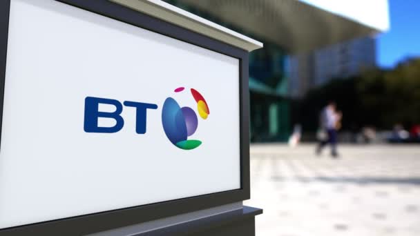 Tablero de señalización con logotipo del Grupo BT. Centro de oficina borrosa y gente caminando fondo. Representación editorial 4K 3D — Vídeos de Stock