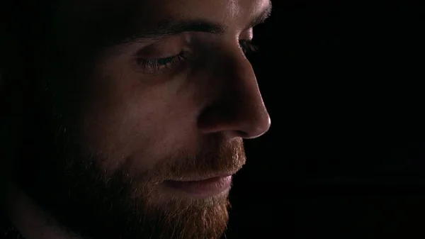 Profile view of focused intelligent bearded young man using his tablet computer. Device lighting glow, dark background — Stock Photo, Image