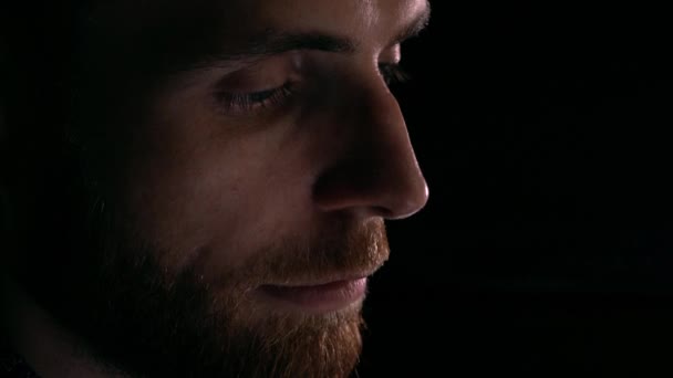 Vista de perfil de un joven barbudo inteligente enfocado usando su tableta. Iluminación del dispositivo brillo, fondo oscuro. 4K tiro de cerca — Vídeo de stock