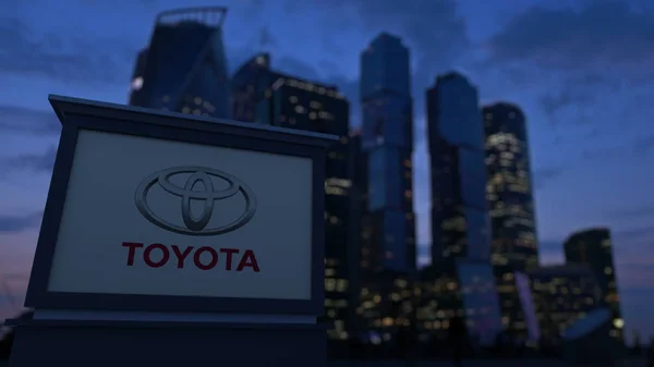 Уличная вывеска с логотипом Toyota в вечернее время. Размытые данные о небоскребах в деловом районе. Редакционная 3D рендеринг — стоковое фото