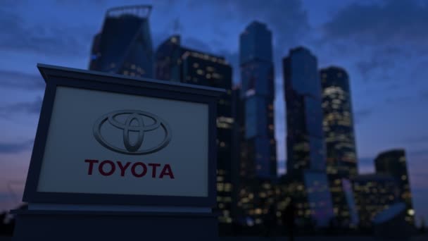 Tablero de señalización de calle con logotipo de Toyota en la noche. Rascacielos distritos de negocios borrosa fondo. Clip editorial 4K — Vídeos de Stock