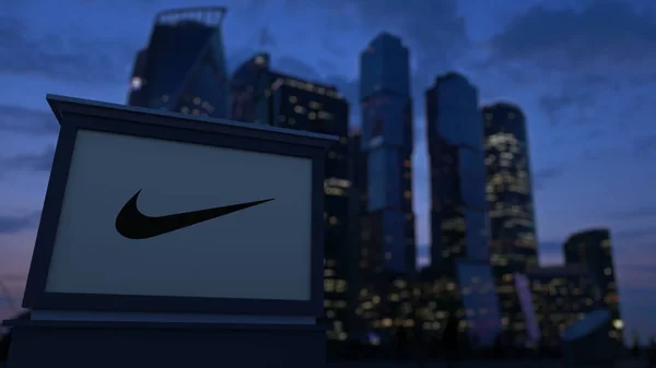 Segnavia stradale con logo Nike la sera. Sfondo sfocato grattacieli quartiere degli affari. Rendering editoriale 3D — Foto Stock