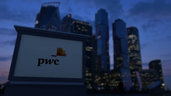 Уличная вывеска с логотипом PricewaterhouseCoopers PwC вечером. Размытые данные о небоскребах в деловом районе. Редакционная 3D рендеринг — стоковое фото
