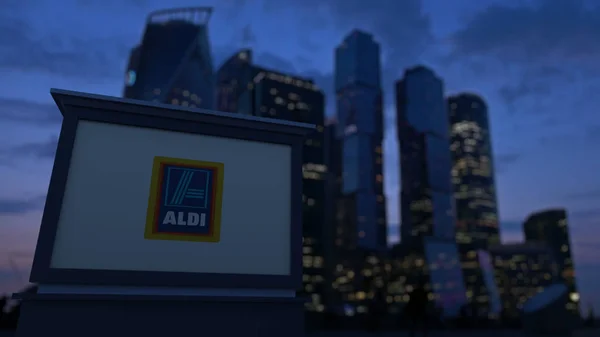 Cartelera con el logotipo de Aldi por la noche. Rascacielos distritos de negocios borrosa fondo. Representación Editorial 3D — Foto de Stock