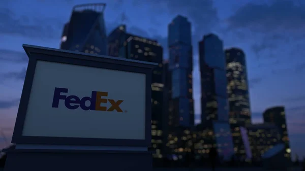 Уличная вывеска с логотипом FedEx вечером. Размытые данные о небоскребах в деловом районе. Редакционная 3D рендеринг — стоковое фото