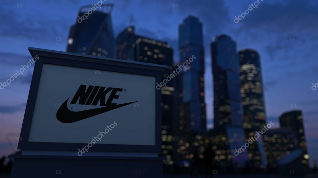 Street signage board with Nike inscription and logo in the evening. Blurred business district skyscrapers background. Editorial 3D United States
