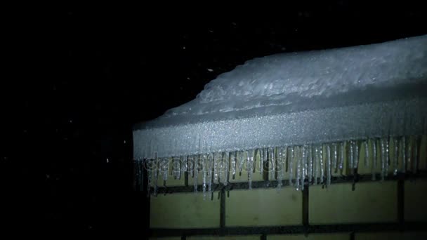 れんが造りの建物と夜スーパー スロー モーションで降雪の屋根の上のつららを撮影します。 — ストック動画