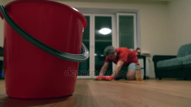 Cubo rojo y hombre desenfocado en camiseta roja limpiando la habitación. Disparo 4K — Vídeos de Stock