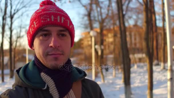 Uomo pensieroso in cappello rosso a piedi nel parco invernale 4K stabilizzato colpo di snorricam — Video Stock