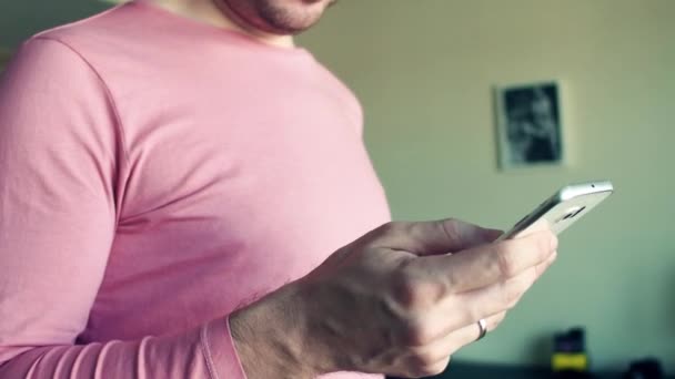 MOSCÚ, RUSIA - 20 de noviembre de 2016. Hombre de rosa camiseta de desplazamiento Instagram aplicación en su teléfono inteligente en casa. 4K primer plano steadicam disparo — Vídeo de stock