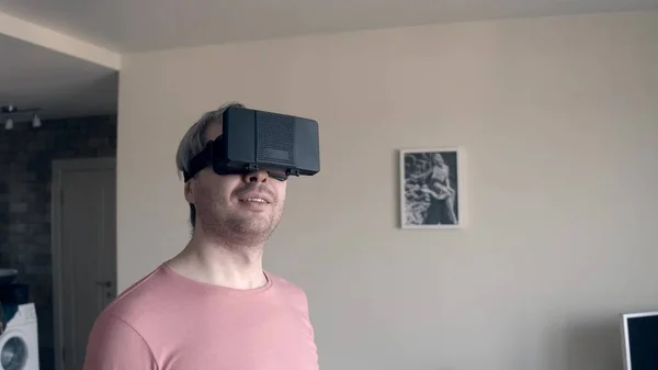 Bonito homem feliz em camiseta rosa usando seu fone de ouvido VR para celular em casa. Óculos de realidade virtual acessíveis em ação — Fotografia de Stock
