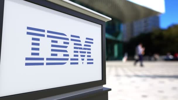 Tablero de señalización con logotipo de IBM. Centro de oficina borrosa y gente caminando fondo. Representación editorial 4K 3D — Vídeos de Stock