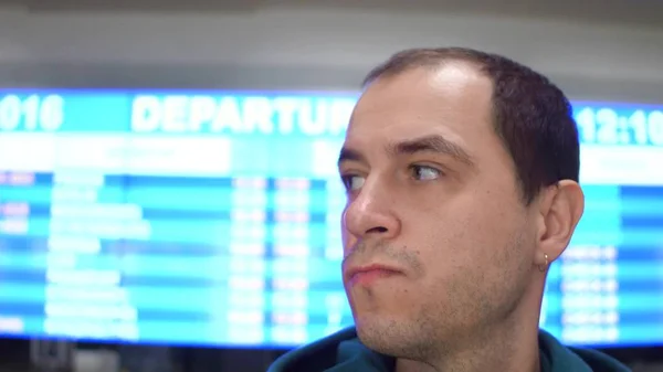 Worried caucasian man looking around near airport departure board. Tourism, travel, waiting concepts