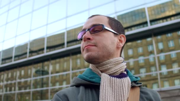 Intelligent caucasian man wearing black rim glasses looks around in city business district. 4K steadicam video — Stock Video