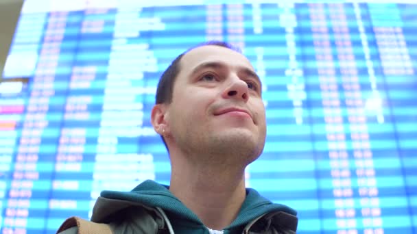 Homme caucasien excité regardant autour du tableau de départ de l'aéroport. Tourisme, voyages, concepts d'attente. Vidéo 4K steadicam à faible angle — Video