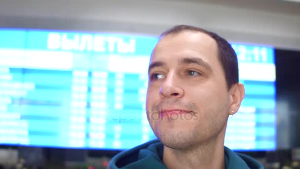 Glücklicher kaukasischer Mann, der sich in der Nähe der Flugplantafel des Flughafens umsieht. Tourismus, Reisen, Wartekonzepte. 4k Niedrigwinkel-Steadicam-Video — Stockvideo