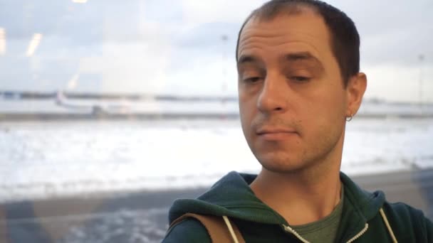 Кавказький чоловік в аеропорту проти вікно до аеродрому. Туризм, подорожі, очікування концепцій. 4 к відео — стокове відео