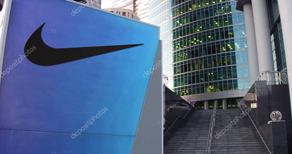 Street signage board with Nike logo. Modern office center skyscraper and stairs background. Editorial 3D rendering United States