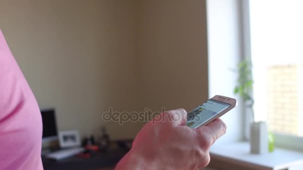 MOSCÚ, RUSIA - 20 de noviembre de 2016. Hombre de camiseta rosa desplazándose aplicación de Instagram en su teléfono móvil en casa. 4K primer plano steadicam video — Vídeo de stock