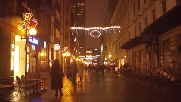 WARSAW, POLONIA - 28 DE NOVIEMBRE DE 2016. La gente camina por la calle iluminada cafés y tiendas por la noche. Luces y decoraciones navideñas. Ciudad europea 4K steadicam video — Vídeos de Stock