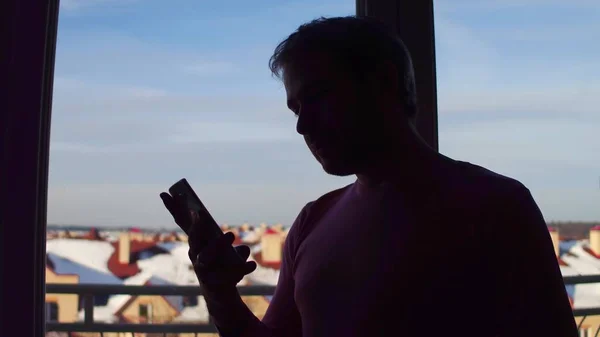 Силуэт человека, использующего свой мобильный телефон возле большого окна — стоковое фото