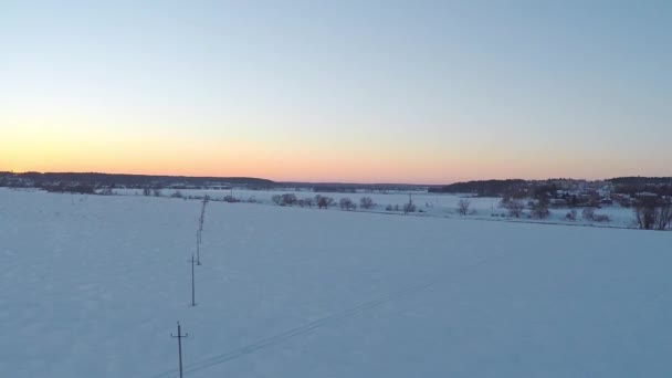 Воздушное видео пилонов малых линий электропередач и далёких домов на закате зимой — стоковое видео