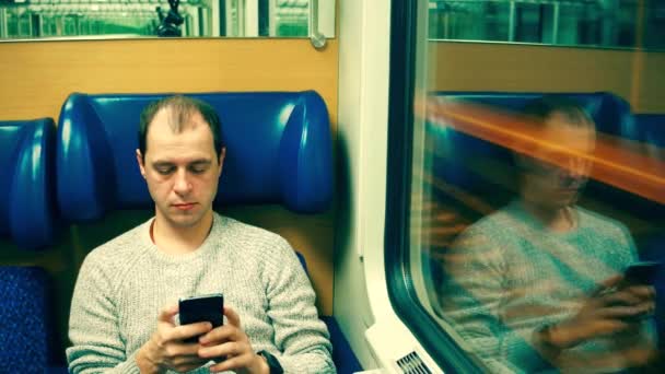 Un uomo caucasico concentrato che digita messaggi nel suo cellulare su un treno. Moderne tecnologie di comunicazione wireless. Video 4K — Video Stock