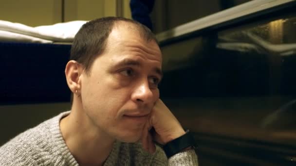 Вдумчивый человек с сережкой, путешествующий на поезде ночью. 4К выстрел — стоковое видео