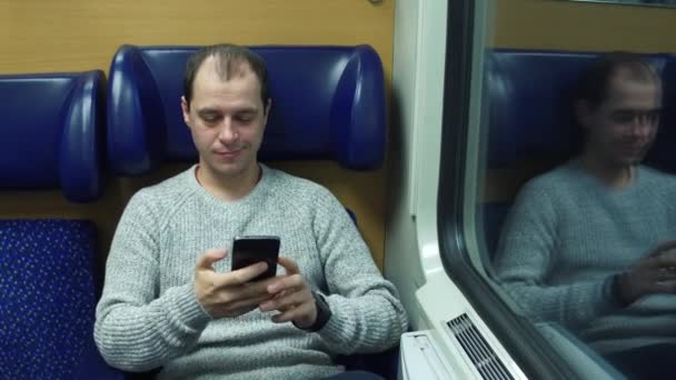 Un uomo che si siede su un treno e scrive messaggi sul cellulare. Moderne tecnologie di comunicazione wireless. Video 4K — Video Stock