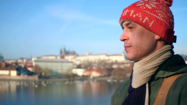 Σκεπτικός ο άνθρωπος στο κόκκινο πλεκτό καπέλο περπάτημα στο ηλιόλουστο ποταμού enbankment στην Πράγα. 4 k steadicam βίντεο — Αρχείο Βίντεο