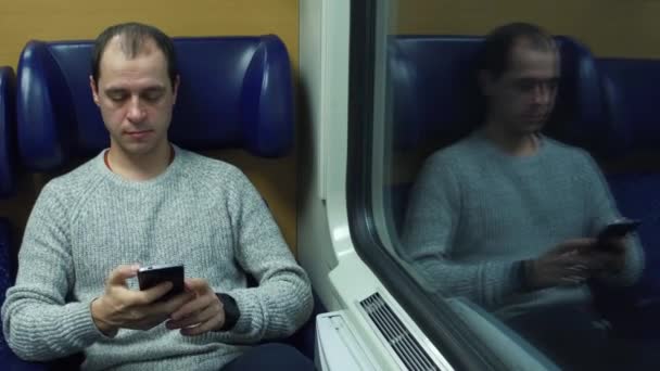 Gelukkig man zijn zetel in een trein nemen en verzenden van berichten in zijn mobiele telefoon. Moderne draadloze communicatietechnologieën. 4k video — Stockvideo