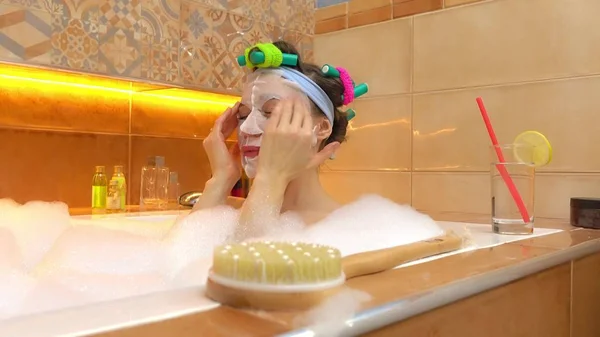 Brünette Frau mit Gesichtsmaske im Schaumbad. Schönheitsbehandlungen zu Hause — Stockfoto