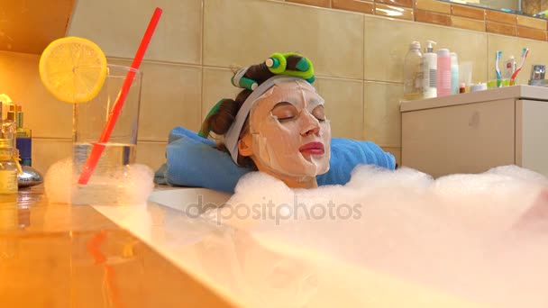 Mulher bonita morena vestindo máscara facial cosmética relaxa no banho espumoso. Tratamento de beleza em casa. 4K tiro — Vídeo de Stock