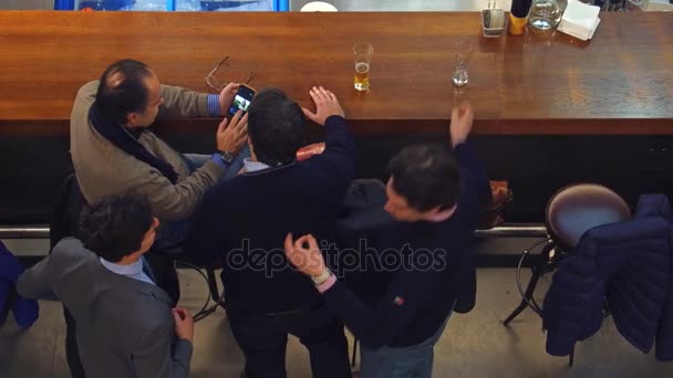 Warsaw, Polen - December, 22, 2016. Midden leeftijd man delen van foto's van vrouw op zijn smartphone met vrienden aan de bar. 4k bekijken above video — Stockvideo