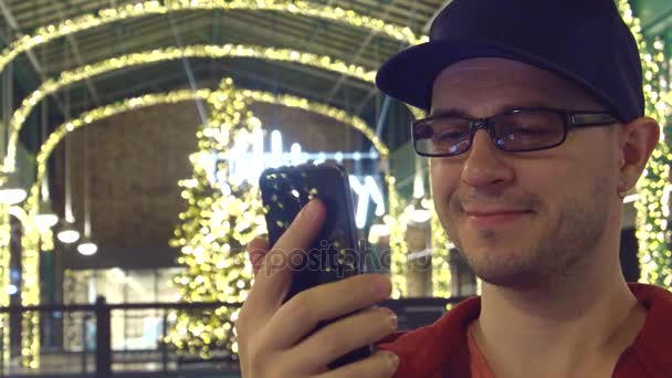 Happy man in black rim glasses watching video on his mobile phone in a Cristmas decorated cafe. 4K video — Stock Video