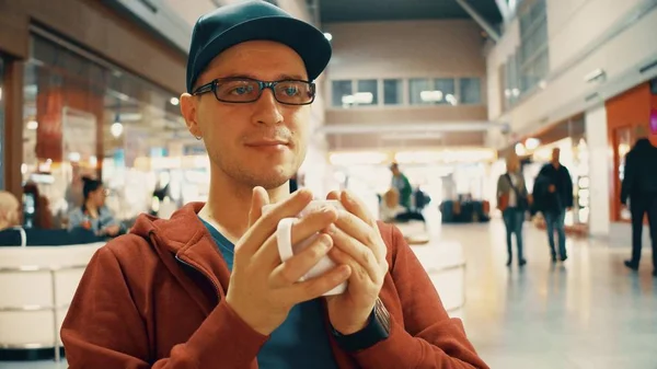 Nerdy man in black rim glasses having big cup of coffee at the airport cafe — Stock Photo, Image