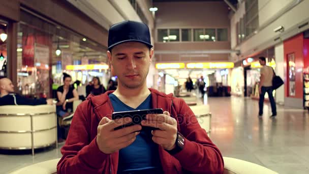 Мужчина-путешественник в красном играет в игру на мобильном телефоне в кафе аэропорта. 4К выстрел — стоковое видео