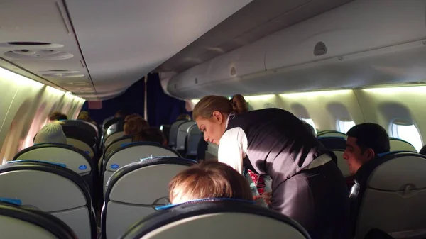 WARSAW, POLONIA - DICIEMBRE, 24. LOT Auxiliar de vuelo femenina en el trabajo y pasajeros de avión en la cabina — Foto de Stock